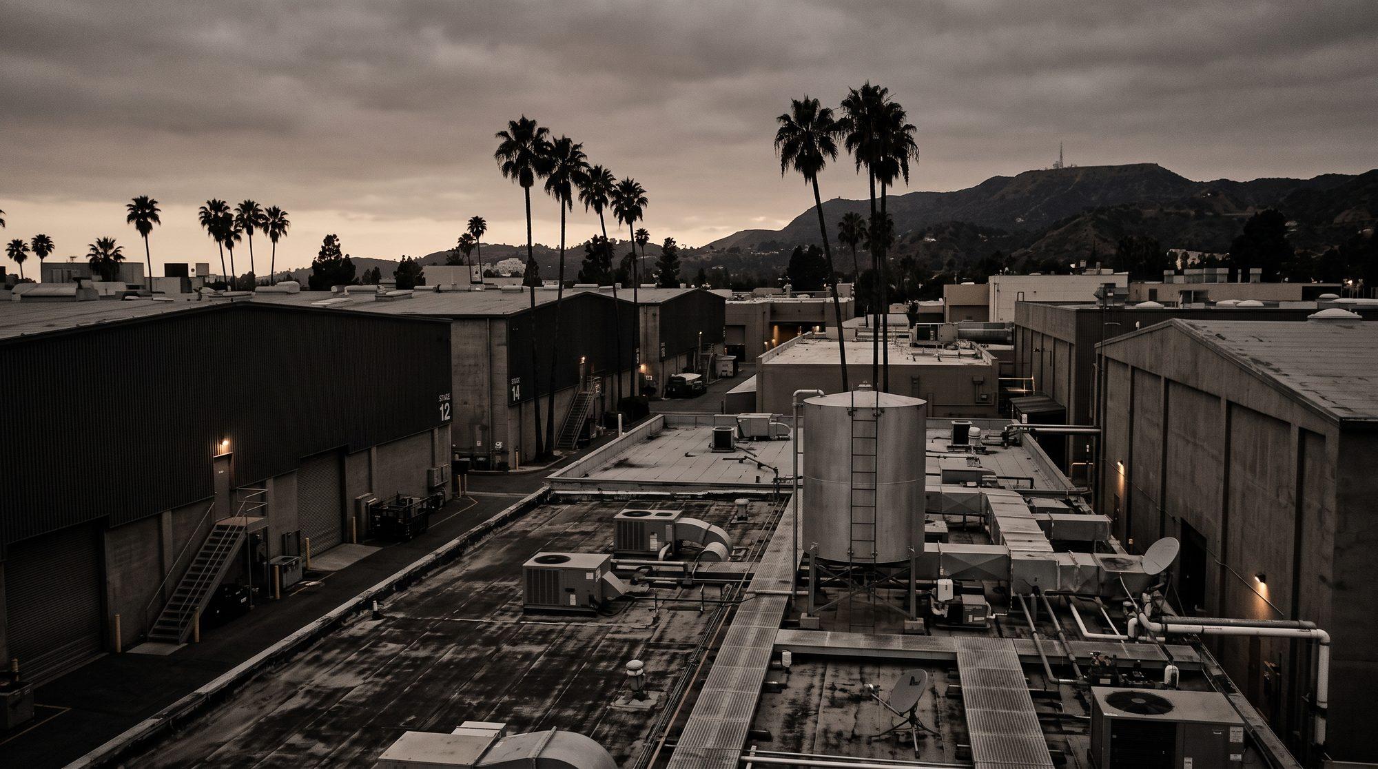 Studio backlot rooftops and soundstage exteriors in Los Angeles at dusk, under an overcast sky.